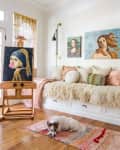 Art-filled room with a cozy bench, fluffy pillows, a dog on a rug, and an easel displaying a painting of a girl with a pearl earring.