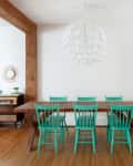 Dining area with wooden table, six turquoise chairs, and a white pendant light, adjacent to a vintage radio console.