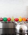 Colorful fruit-shaped kitchen timers on a stove with a silver kettle and utensils.