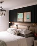 Bedroom with a wooden bed, white bedding, black accent wall, abstract art, and a geometric chandelier.