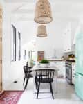 White kitchen with hexagonal tiles, wooden table, black chairs, wicker pendant lights, and a mint green fridge.