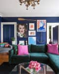 Living room with dark blue walls, green velvet sofa, pink cushions, eclectic wall art, and a map of Europe.