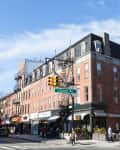 Red brick building on a street corner with shops, fire escapes, and a Clinton Ave street sign.