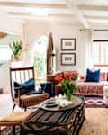 Cozy living room with a white sofa, colorful cushions, leather armchair, tulips on a coffee table, and large windows.
