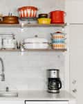 Kitchen with open shelves displaying colorful cookware, dishes, and a coffee maker on the counter.