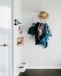 Entryway with wall hooks holding hats, bags, and jackets, a wire basket, and pet bowls near a staircase with glass railing.