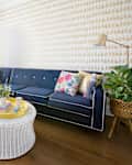 Navy blue sectional sofa with floral pillows, white wicker coffee table, and a potted plant in a bright living room.