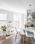 Modern kitchen with gray cabinets, white island, three bar stools, stainless steel appliances, and mint green pendant lights.