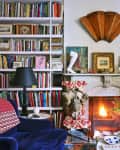 Cozy living room with a fireplace, bookshelves, blue velvet chair, red-patterned throw, and tulips on a coffee table.