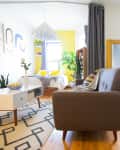 Bright living room with gray sofa, geometric rug, white desk chair, and yellow accents.