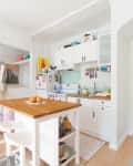 A white kitchen in a studio apartment with mint green backsplash and a butcher block island