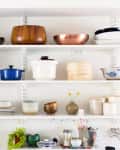 Open kitchen shelves with assorted bowls, pots, plates, and decorative items.
