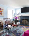 Living room with pink chairs, glass coffee table, blue fireplace, abstract art, and decorative vases on shelves.