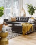 Modern living room with gray sectional sofa, mustard throw, plants, hanging chair, and a guitar by the fireplace.