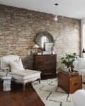 Living room with exposed brick wall, white sofas, wooden chest, and a potted plant on a patterned rug.