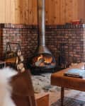 Cozy living room with wood paneling, brick fireplace, wooden coffee table, and a potted plant on a sideboard.
