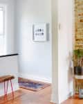 Hallway with arched entry, wooden floor, colorful rug, framed photos, and a potted plant next to a brick wall.