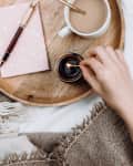 Cozy flatlay with wooden tray, cup of coffee or cocoa, candle, notebooks on white sheets and blankets