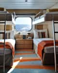 Cruise ship cabin with bunk beds, orange accents, striped pillows, and a window view of the ocean.