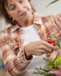 Woman arranging a colorful bouquet with pink lilies, purple irises, and greenery using pruning shears.