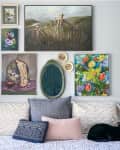 Gallery wall of paintings above bed with pillows and cat