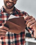 Close up of young man opening envelope and smiling while standing indoors