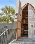 Large wooden double doors with a weathered finish, leading to a home entrance with a lantern and palm trees nearby.
