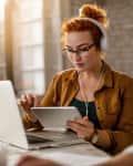 Woman sitting at desk using tablet wearing glasses and headphones