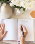 Hands writing in gratitude journal with cup of coffee on table