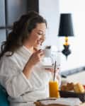 Woman sitting in bed at hotel eating breakfast in bed room service