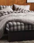 Plaid bedding set on a bed with wooden headboard and textured rug.