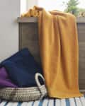 Yellow towel draped over a wooden ledge, with blue and purple towels in a woven basket on a striped rug.
