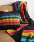 Crocheted pillow and blanket with rainbow stripes on a tan sofa, next to a green plant.