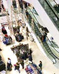 Shoppers and escalators in a busy department store with clothing displays and holiday decorations.