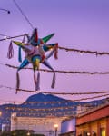 Colorful piñata hanging over a street with festive lights and buildings at dusk.
