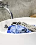 Clothes soaking in a white bathroom sink with a chrome faucet.