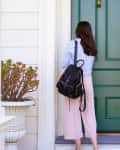 Back view of a woman carrying a backpack back to home using a key to open her front door