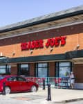 Trader Joe's storefront with red brick exterior, parked cars, and a person entering the store.