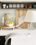 Kitchen counter with lemons in a bowl, cutting boards, a brass faucet, and a pleated lamp.