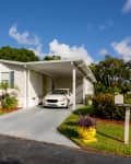 Single-story home with a carport, white car, colorful plants, and a mailbox in a sunny neighborhood.