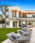 Modern two-story house with pool, patio, spiral staircase, and lounge chairs on a lawn.