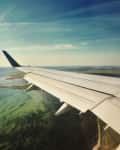Airplane wing over coastline with green and blue water, under a clear sky.
