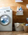 Laundry room with a front-loading washing machine, wooden walls, shelves with folded towels, and wicker baskets.