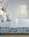 Attic bedroom with floral bed, brass lamps, wicker baskets, and blue striped chair.