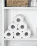 Bathroom shelf with stacked toilet paper rolls, soap dispensers, a wicker basket, and a green decorative stone.