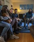 Group of six people sitting in a living room, one in a wheelchair, with blue abstract art on the wall.