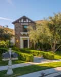 Two-story house with stone facade, arched driveway, manicured hedges, and two mailboxes on a sunny day.