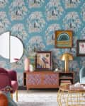 Eclectic living room with teal palm wallpaper, colorful art, pink and teal furniture, and a gold lamp on a wooden console.