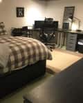 Bedroom with plaid bedding, string lights, desk with chair, and wall decor including a clock and framed letter "K".