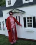 Woman in red pajamas standing beside a white playhouse with black shutters and a porch.